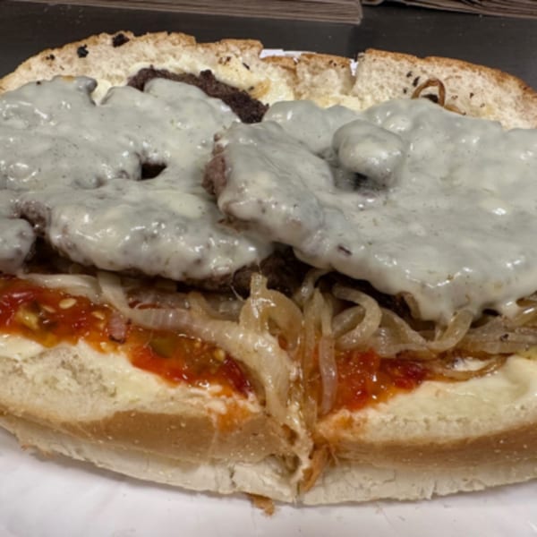 A close-up of a cheesesteak sandwich from Eddies Pizza & Catering, topped with melted cheese, onions, and sauce.
