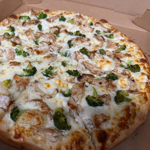 A whole Eddies Pizza & Catering chicken and broccoli pizza with white sauce in a cardboard box.