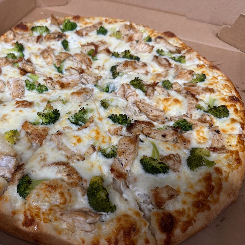 A whole Eddies Pizza & Catering chicken and broccoli pizza with white sauce in a cardboard box.