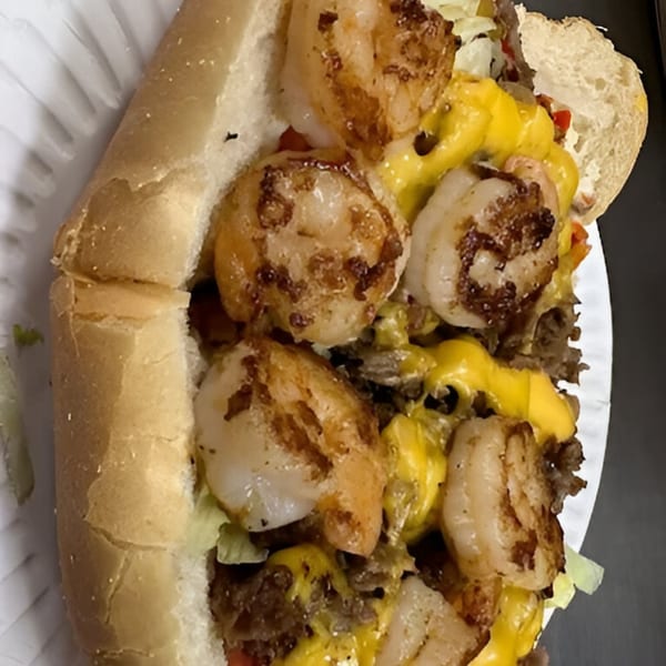 A close-up of a shrimp and steak sub with melted cheese and vegetables on a white paper plate.