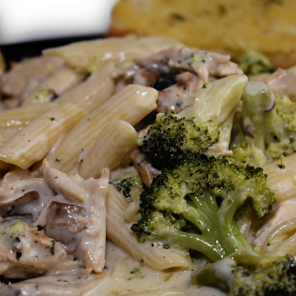 Creamy penne pasta with chicken, mushrooms, and broccoli florets, served with garlic bread.